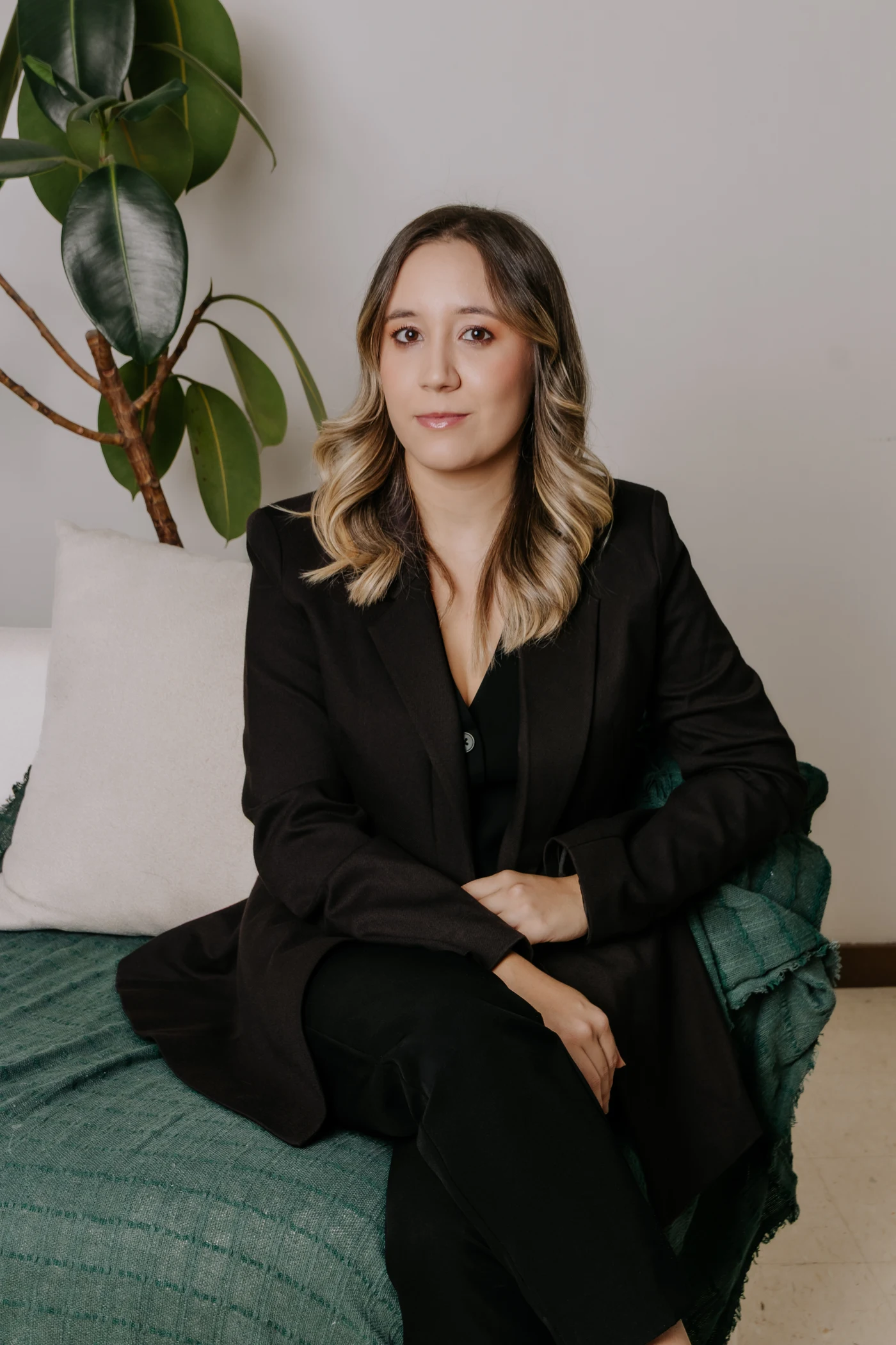 Dra. Carolina Zanetti sentada em uma poltrona verde, com blazer preto